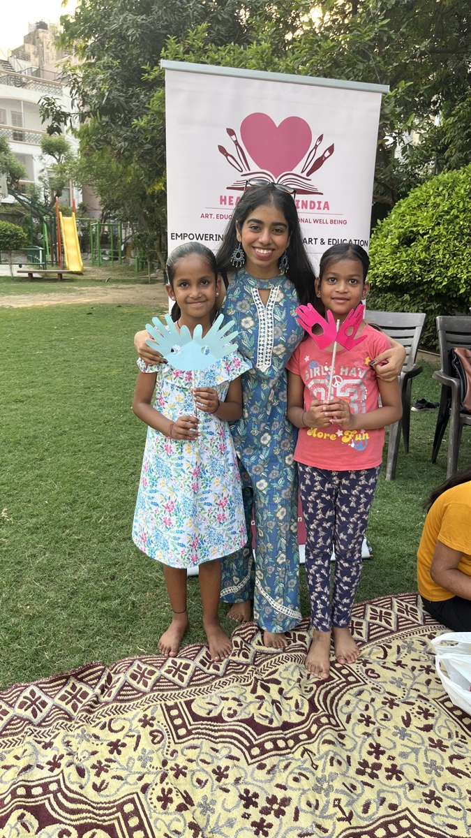 A Heart Arts facilitator outdoors with two young girls holding the paper hands they cut out